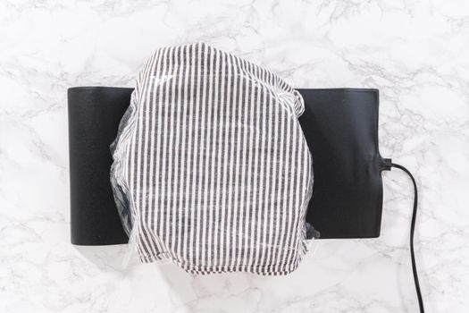 Flat lay. Rising brioche dough on a glass mixing bowl under a kitchen towel.