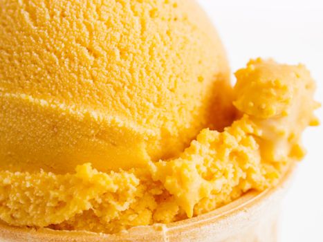 Scoop of gourmet pumpkin gelato in cake cone on white background.
