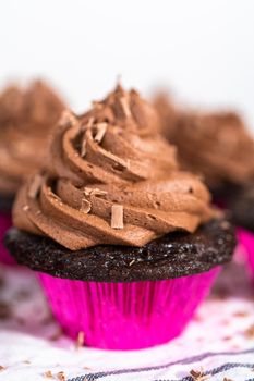 Piping chocolate ganache frosting on top of chocolate cupcakes.