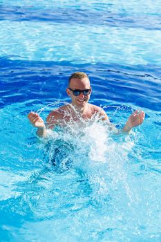 Young attractive man in sunglasses is resting in the pool on summer vacation. The guy in the pool by the hotel