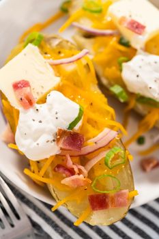 Pressure Cooker Baked Potatoes. Garnished large baked potatoes with butter, sour cream, cheese, and bacon bits on a white plate.