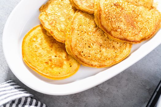 Freshly made pumpkin pancakes on a white serving plate.
