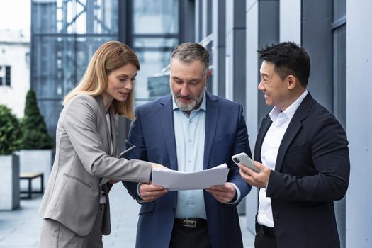 Three businessmen outside office building with documents discussing plans, businessmen and businesswoman having fun chatting and talking, diverse business group in business suits