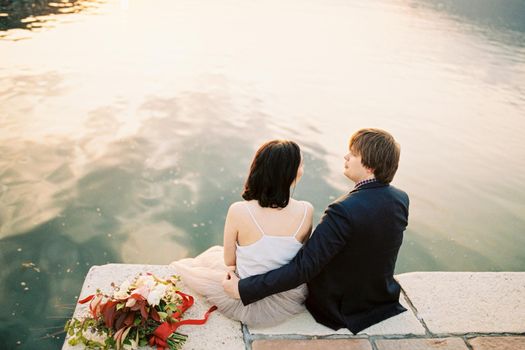 Bride and groom hugging sitting on the pier by the sea. High quality photo