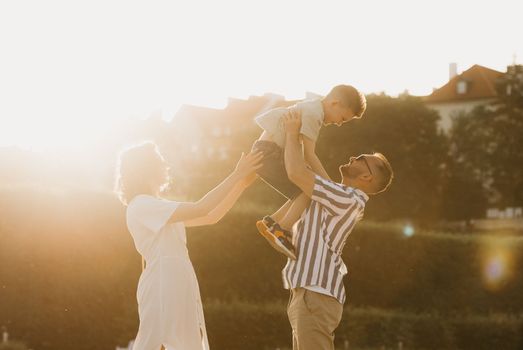 Father, mother and son are having fun in an old European town. Happy family in the evening. Dad is throwing his little boy up.