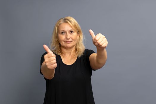 Pretty caucasian blonde woman in casual clothes approving doing positive hand gesture, thumbs up smiling and happy for success. Winning gesture. Isolated on gray studio background