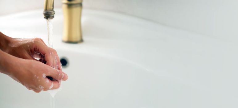 A young girl washes her hands thoroughly with soap under water in the bathroom, close-up view.