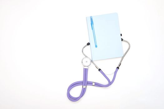 A lilac phonendoscope lies on a table with a notepad and a pen, view from above. High quality photo