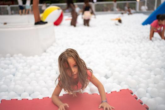 Happy little girl playing white plastic balls pool in amusement park. playground for kids. Active leisure for children.