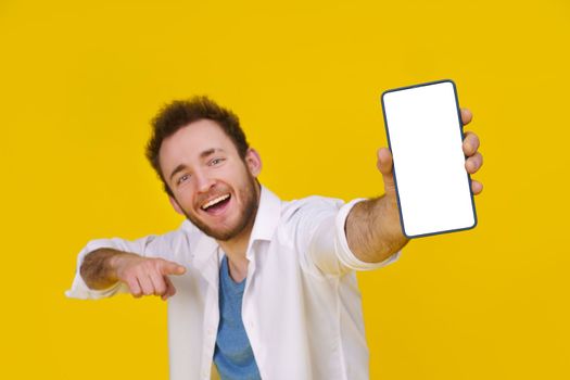 Great offer. Young happy man holding smartphone showing a white empty screen and exciting to win isolated over yellow background, celebrating success. Product placement. Mobile App Advertisement.