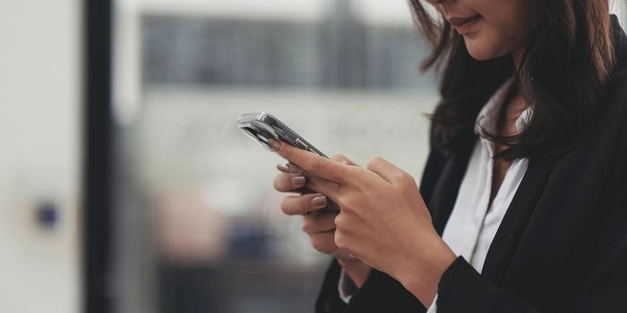 Closeup of female hands using modern smartphone device near urban office, focus on cellphone, social network and communication concept