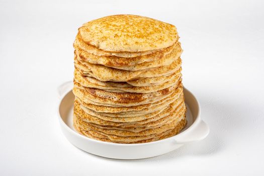 Stack of freshly baked pancakes lie in white ceramic form. Pancake week. Russian kitchen. Selective focus.