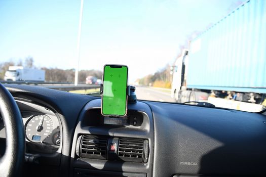 Smartphone with green screen in windshield holder in car interior, road navigation and maps. High quality photo