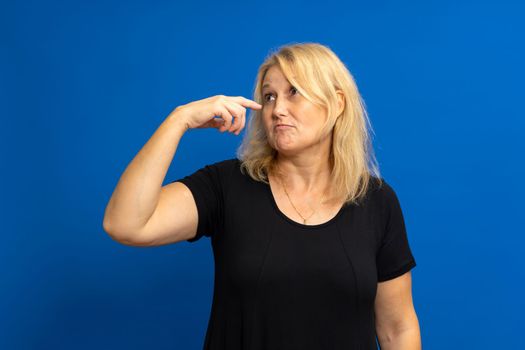Photo of crazy amazed woman pointing index finger at herself, impressed, chooses news, isolated over blue tinted background