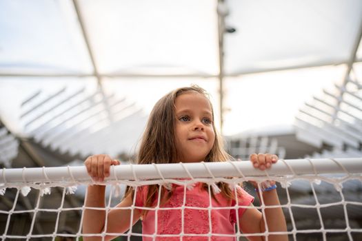 Little girl lean on net looking away. Lost caucasian child. Female kid unhappy when playground is closed on quarantine