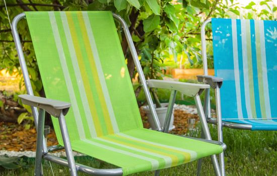 Two garden folding chairs stand in the shade under a tree on a hot summer day in the garden, close-up.