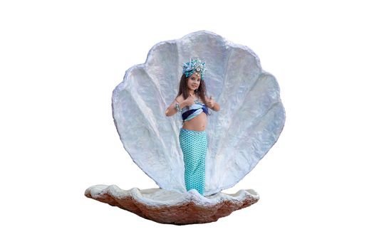 A cute little girl in a mermaid costume stands in a large sea shell, holds her thumbs up, isolated, on a white background