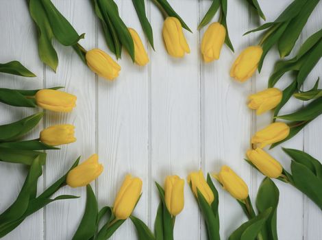 Yellow tulips are laid out on a white wooden table. Space for text. Mockup. Spring flatley.