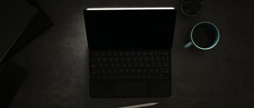 Digital tablet with wireless keyboard and cup of coffee on black wooden table.