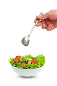 White bowl of salad with fresh cucumbers, tomatoes, iceberg salad leaves and male hand pouring oil with spoon over salad isolated on white background