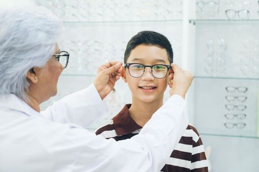 Smart young buy student in striped polo t-shirt happy trying out, testing, and choosing new eyeglasses for study with professional optician supervising at optical store.