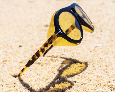 Unusual yellow sunglasses stuck in the sand on the beach close up