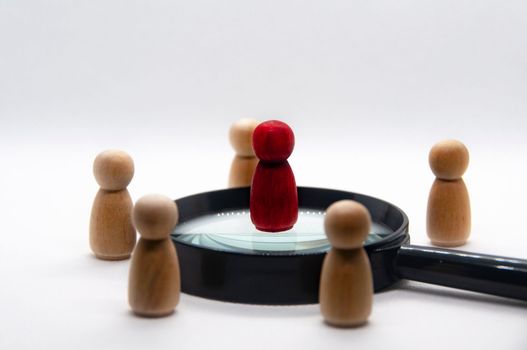 Red wooden doll on top of magnifying glass surrounded with other wooden figure. leadership concept