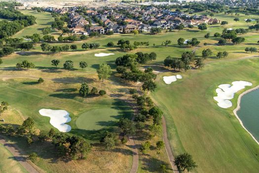 Aerial overview of luxury villas located around green zone and golf playground in the summertime