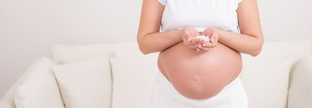 A faceless pregnant woman is holding a handful of white pills