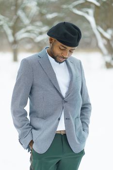Sad african man stay in winter in snowy park. Young man in beret posing for camera outdoor. High quality photo