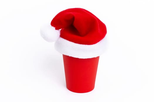 Red paper cup with red Santa Claus cap on, standing on a white background, isolated.