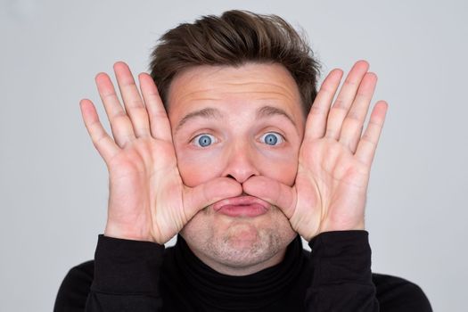 Funny young Caucasian man grimacing, having stupid and ridiculous facial expression.