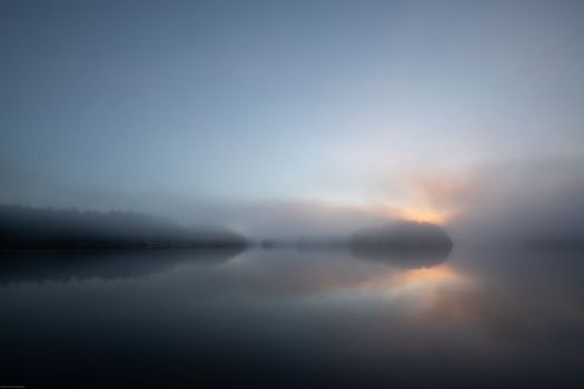 Morning fog with sun peeking through clouds and reflection in the harbour, Blunden Harbour, British Columbia, Canada. Fog on a harbour