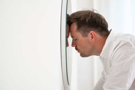 Unhappy businessman leaning on mirror trying to calm down getting bad news. Midlife crisis
