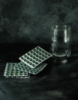 Chlorella or spirulina tablets and a glass of water on dark concrete background