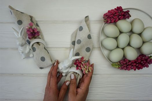 Women's hands decorate a napkin for the Easter table. There are Easter eggs in the plate.