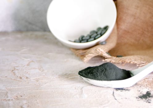 Spirulina tablets and powder in a white spoon and bowl on brown napkin