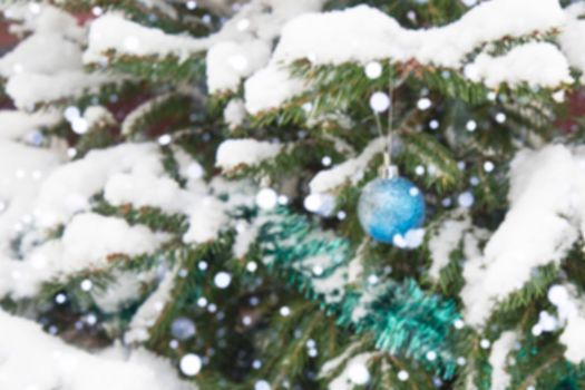 The background is without sharpness, there is no focus. Winter, festive, Christmas background. A Christmas tree decorated with toys and tinsel. Snowfall. Falling snow. Bokeh.