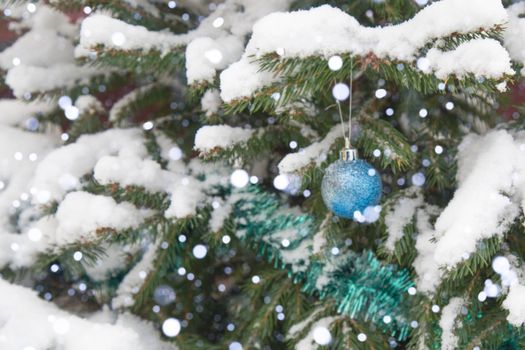 The background is without sharpness, there is no focus. Winter, festive, Christmas background. A Christmas tree decorated with toys and tinsel. Snowfall. Falling snow. Bokeh.
