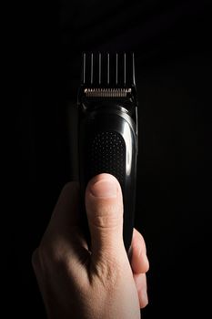 Close-up of Electric shaver machine with nozzle in hand on black background, copy space, vertical.
