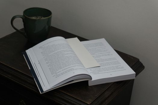 Open book and coffee cup on antique bedside table