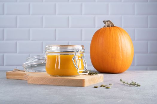 Pumpkin puree soup with pumpkin seeds and thyme in a glass jar on a wooden kitchen board. Ripe pumpkin. Healthy diet. Selective focus.