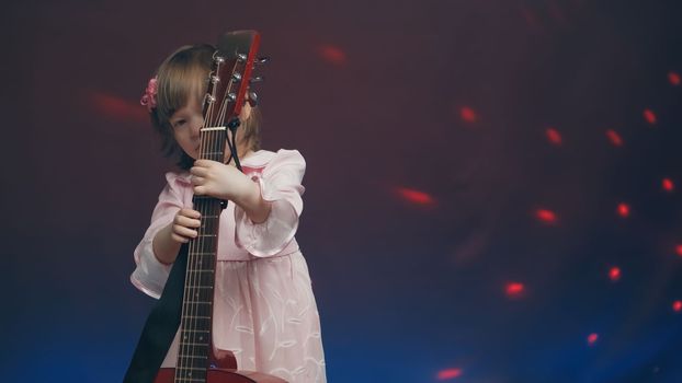 Cute little girl stands on stage in vintage dress and plays an acoustic guitar like a counter bass or cello. The concept of performing the author jazz and blues music. Hobbies and art among children