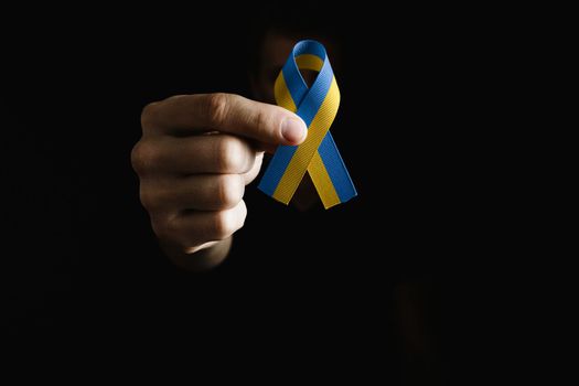 male hand holds yellow and blue ribbon on dark background. concept needs help and support, truth will win