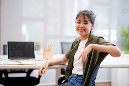 Close up of Young asian businesswoman working hard at the office using laptop data graphs, planning for improvement, analyzing and strategizing for business growth smiling at camera. Business concept.