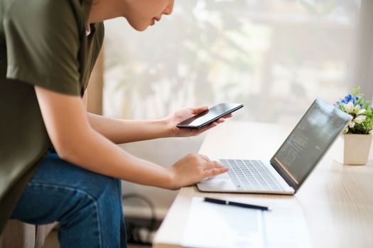 Young asian businesswoman uses a mobile phone to contact a customer, working hard at the office using laptop data graphs, planning for improvement, analyzing and strategizing for business growth. Business concept