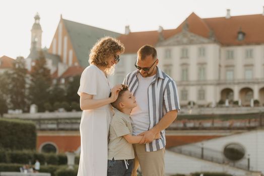 Father, mother and son are hugging in an old European town. Happy family in the evening. Mommy is stroking her little boy's head in the background of the palace at sunset.
