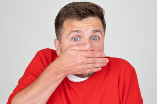 Portrait of a shocked young caucasian man covering his mouth with hands.