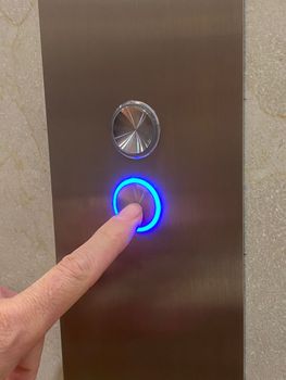 finger pressing elevator button down in blue light.