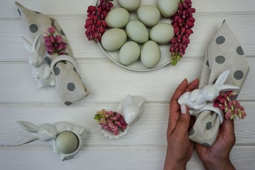 Women's hands decorate a napkin for the Easter table. There are Easter eggs in the plate.